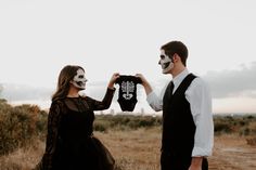 a man and woman in skeleton makeup holding up a black box with a skeleton on it