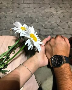 two people holding hands with flowers on the ground in front of brick wall and cobblestone walkway