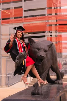 a woman in a graduation cap and gown posing next to a statue of a tiger