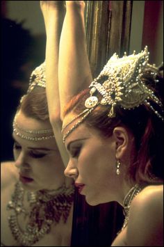 two women wearing headpieces and jewelry in front of a mirror with one woman's face