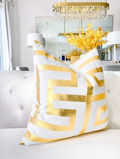 two white and gold pillows sitting on top of a couch next to a chandelier