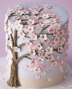 a cake decorated with pink flowers and branches on a white tableclothed surface in front of a purple background