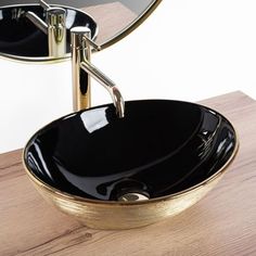 a black and gold bowl sink on top of a wooden counter with a mirror above it