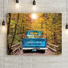 an old blue truck parked on a bridge in the woods with trees and leaves around it