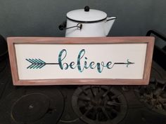 a wooden sign that says believe with an arrow on it and a pot next to it