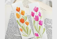 two bookmarks decorated with watercolor flowers on top of an open book, next to each other