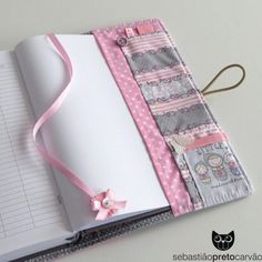 an open notebook with a pink ribbon attached to the front and back cover, sitting on top of a table