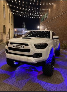 a white toyota truck parked in front of a brick building with blue lights on it