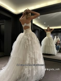 a woman in a wedding dress looking at herself in the mirror with her back to the camera