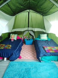 two beds in a tent with blue sheets and pillows on the floor, under a green canopy