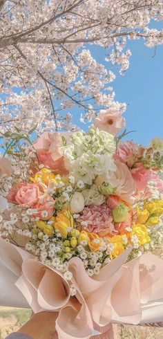 a person holding a bouquet of flowers under a tree with blue sky in the background