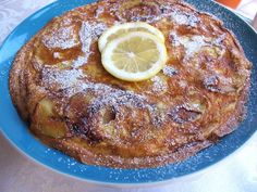 a blue plate topped with pancakes covered in powdered sugar and a lemon wedge on top