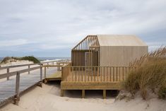 a small wooden building sitting on top of a beach next to tall grass and sand