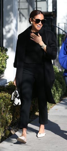 a woman in black is walking down the street with her hand on her chest and wearing sunglasses