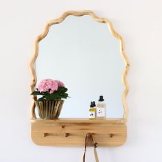 a wooden shelf with a mirror and flowers on it next to a handbag hanging from the wall