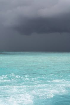 the ocean is very blue and green under a dark sky with storm clouds above it