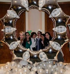 a group of women standing next to each other in front of a mirror with balloons