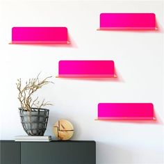 three pink shelves are on the wall above a vase with flowers and a potted plant