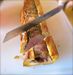 a knife cutting into a sandwich on top of a white plate with meat in it