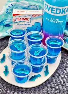 blue liquid in plastic cups on a plate next to a bottle of soda and napkins