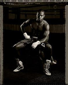 a black and white photo of a man sitting in a boxing ring with his hands on his knees