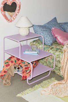 a purple table sitting on top of a bed next to a white lamp and pillows