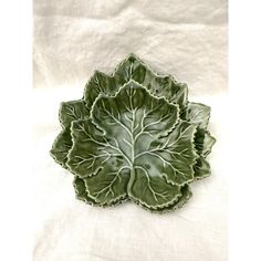 a green leaf shaped dish sitting on top of a white cloth