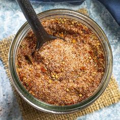 a glass jar filled with spices on top of a blue table cloth next to a wooden spoon