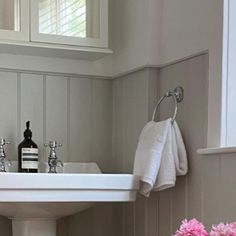 a white sink sitting under a bathroom window next to a vase with flowers in it