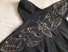 an image of a butterfly on a black shirt that is laying on a bed with white sheets