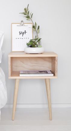 a small wooden table with a plant on it and a calendar next to the bed