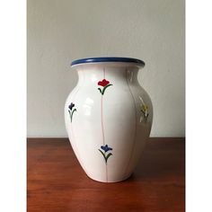 a white vase sitting on top of a wooden table with flowers painted on the side