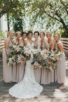 a group of women standing next to each other on a wooden bridge holding bouquets