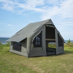 a tent is set up on the grass by the ocean with its door open and windows closed