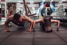 a man and woman doing push ups in a gym