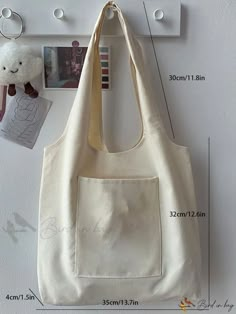 a white bag hanging on the wall next to a stuffed animal and other items with measurements