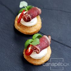 two small appetizers with meat and cheese on crackers are sitting next to each other