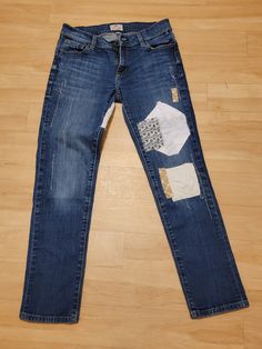 a pair of blue jeans with patches on them sitting on top of a wooden floor