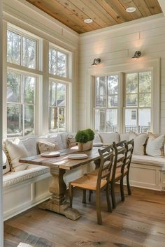 a dining room table and bench in front of two large windows with wooden beams on the ceiling