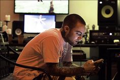 a man sitting in a chair looking at his cell phone while playing music on the computer