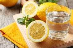 a glass of water with lemons and mint on a cutting board