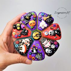 a hand holding a multicolored brooch with halloween decorations on it