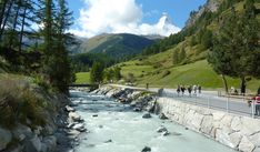 people are standing on the side of a bridge next to a river and some mountains