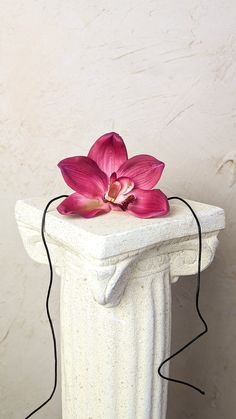 a pink flower sitting on top of a white vase next to a power cord attached to it