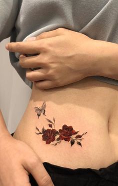 a woman's stomach with red roses and butterflies on her side, while she is showing off her tattoo