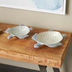 two white bowls sitting on top of a wooden table next to a framed painting in a room