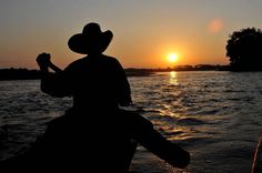 the silhouette of a person in a cowboy hat on a boat watching the sun go down