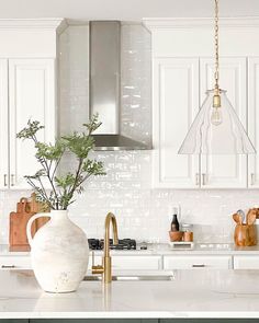 a white kitchen with green cabinets and gold accents on the countertop, along with a large vase filled with greenery