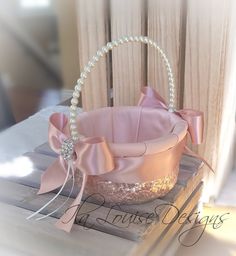 a small pink basket with pearls on the side and a bow around the handle is sitting on a table