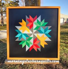 a black and yellow sign with colorful geometric designs on it in the grass next to a tree